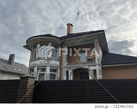 Residential building under construction with exposed brick and plaster, showcasing architectural details and a cloudy sky, representing home renovation and development process 132462162
