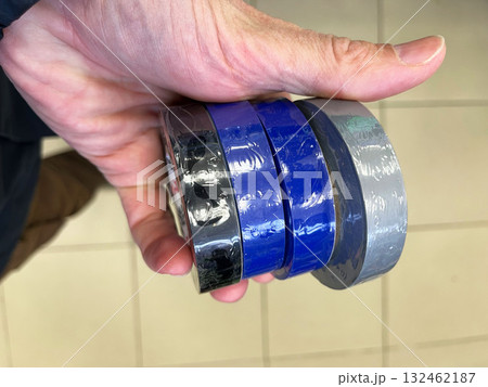 Hand holding multiple rolls of colorful adhesive tape including blue, gray, and black, showcasing various textures and finishes, ideal for crafting and repair projects Hand holding multiple rolls of colorful adhesive tape including blue, gray, and black, showcasing various textures and finishes, ideal for crafting and repair projects 132462187