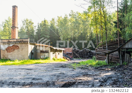 Abandoned industrial site with weathered buildings, a tall chimney, and stacked logs surrounded by lush greenery, showcasing a blend of nature and decay in a serene environment Abandoned industrial site with weathered buildings, a tall chimney, and stacked logs surrounded by lush greenery, showcasing a blend of nature and decay in a serene environment 132462212