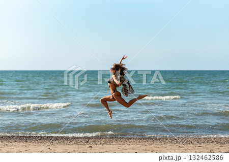 Beach girl leap, Joyful female jumps during sunny day, Vibrant woman executing athletic jump along sunlit shoreline 132462586