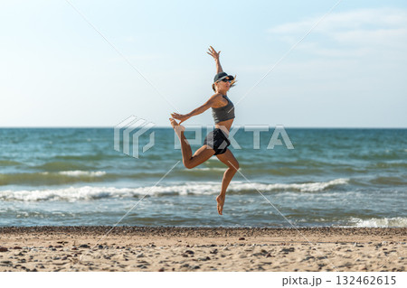 Dynamic leap by shoreline under midday sky, Midair woman performing vigorous coastal workout in bright sunlight 132462615