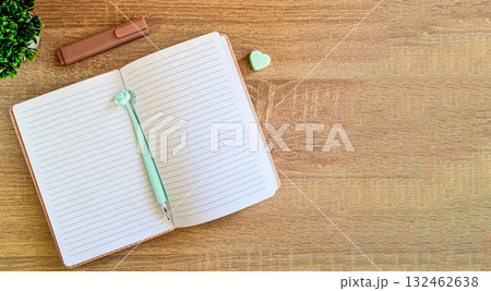 There is an open notebook with a pen and erasers on the wooden surface of the table. 132462638