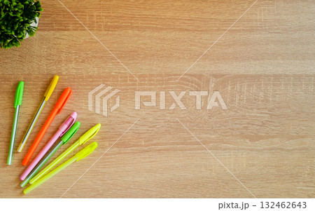 Colored pens lie on a wooden table. A flower is in the background. Colored pens lie on a wooden table. A flower is in the background. 132462643
