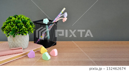 On the wooden tabletop lies a notepad with a marker and erasers, a pen stand, and a flower. On the wooden tabletop lies a notepad with a marker and erasers, a pen stand, and a flower. 132462674