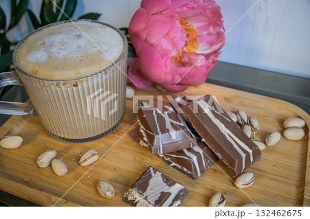 Side view of a cup of coffee with chocolate bars and nuts on a wooden table. Warm natural light creates a cozy atmosphere. 132462675