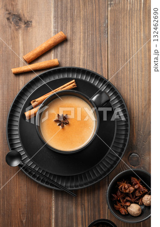 Traditional Indian masala chai tea with milk and spices in a black cup on a dark wooden background Traditional Indian masala chai tea with milk and spices in a black cup on a dark wooden background 132462690