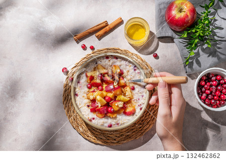 Hand holding spoon in to plate of oatmeal with apple, cranberry and cinnamon on a light background 132462862