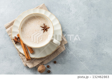 Traditional Indian masala chai tea with milk and spices in a white cup on a light blue background. 132462863