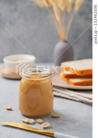 Creamy peanut butter in a jar on a blue background with a scattering of roasted nuts, knife Creamy peanut butter in a jar on a blue background with a scattering of roasted nuts, knife 132462890