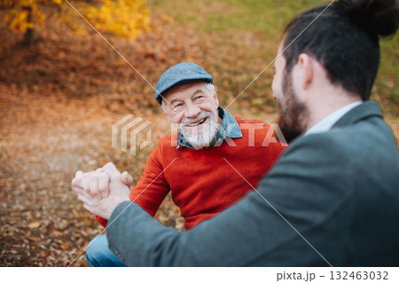 Older man and his son holding hands, sittin on bench by lake and talking. Older man and his son holding hands, sittin on bench by lake and talking. 132463032