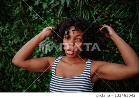 A portrait of a black woman standing against green background of bush leaves. A portrait of a black woman standing against green background of bush leaves. 132463042