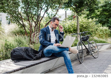 Manager working in urban park, making phone call and typing on laptop. 132463065