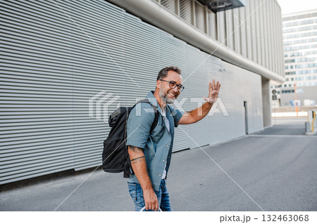 Handsome man with tattoos greeting someone on street. 132463068