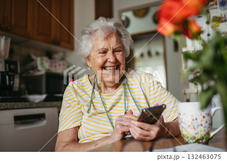 Smiling elderly woman scrolling on phone, browsing internet. 132463075