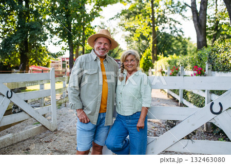 Happy elderly couple standing by white fence. 132463080
