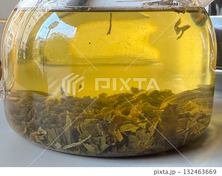 Close-up of tea leaves brewing in glass teapot. Herbal infusion, natural texture, and detail of transparent warmth. Close-up of tea leaves brewing in glass teapot. Herbal infusion, natural texture, and detail of transparent warmth. 132463669