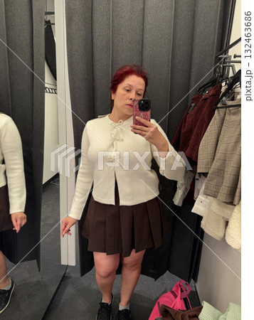 Woman in white cardigan adjusting outfit in fitting room. Style exploration, mirror reflection, and fashion decision moment. 132463686