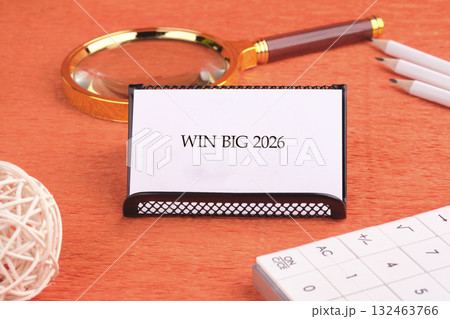 A workspace scene featuring a card that reads Win Big 2026, placed beside a magnifying glass, pens, and a puzzle set, showcasing a creative environment ready for planning 132463766