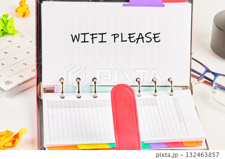 A notebook is open with a request for WiFi written clearly. Surrounding it are colorful sticky notes, a calculator, and a pair of glasses, highlighting a focused work environment 132463857