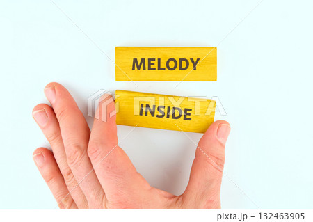 A hand gently reaches for colorful wooden blocks arranged to display the words melody inside. The bright yellow color creates a cheerful atmosphere and inspires creativity A hand gently reaches for colorful wooden blocks arranged to display the words melody inside. The bright yellow color creates a cheerful atmosphere and inspires creativity 132463905
