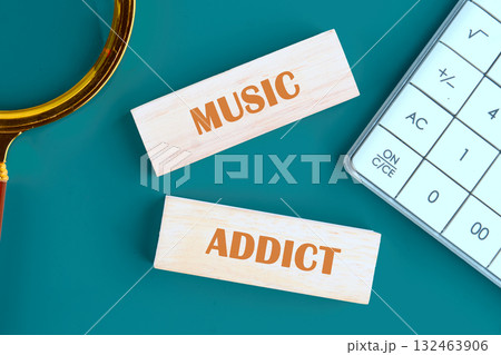 Wooden blocks with the words music and addict lie on a teal surface next to a calculator, highlighting a love for melodies, rhythms, and musical exploration in a creative environment Wooden blocks with the words music and addict lie on a teal surface next to a calculator, highlighting a love for melodies, rhythms, and musical exploration in a creative environment 132463906