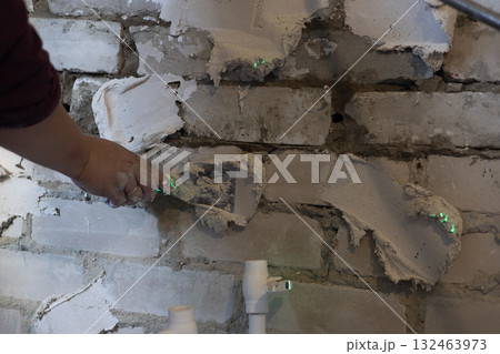 A worker holds a trowel and applies wet plaster or filler mix to an old brick wall during renovation, remodeling, or construction, improving the surface. Preparing a wall with filler. 132463973