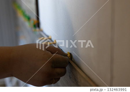 A worker manually installs yellow tile alignment clips to align the tiles with the newly laid tile. These clips ensure precise and professional tiling during renovation work. Laying wall tiles. 132463991