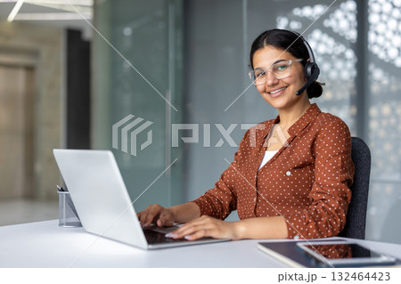 Young woman working in a call center, wearing a headset and spectacles, smiling and typing on a laptop, providing professional customer service and technical support Young woman working in a call center, wearing a headset and spectacles, smiling and typing on a laptop, providing professional customer service and technical support 132464423
