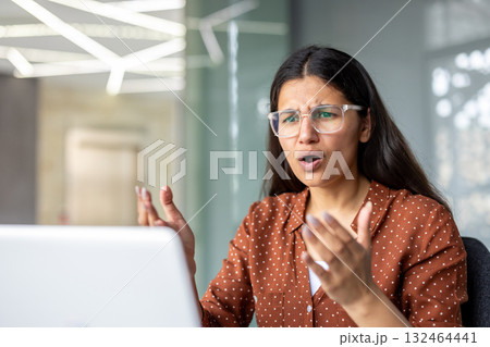 Young woman in glasses feeling shocked and frustrated while working on a laptop, encountering an unexpected business problem in a modern office environment Young woman in glasses feeling shocked and frustrated while working on a laptop, encountering an unexpected business problem in a modern office environment 132464441
