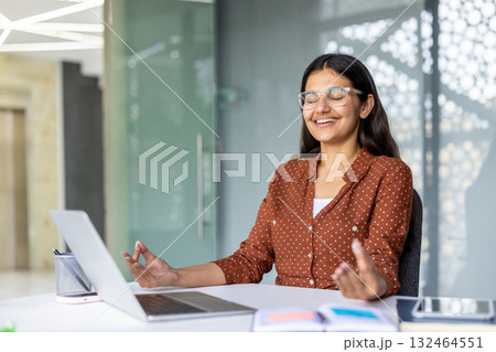 Young indian corporate professional finding inner peace and mindful balance at her office desk, practicing meditation and relaxation in a modern workspace Young indian corporate professional finding inner peace and mindful balance at her office desk, practicing meditation and relaxation in a modern workspace 132464551