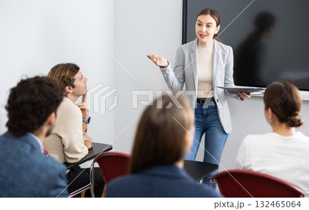 Young woman standing near interactive board and communicating with adult students during advanced training courses in classroom Young woman standing near interactive board and communicating with adult students during advanced training courses in classroom 132465064