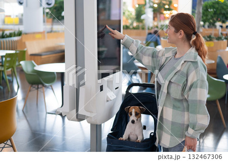Caucasian woman makes a purchase at a self-service counter with a Jack Russell terrier dog in a stroller in a shopping center. Caucasian woman makes a purchase at a self-service counter with a Jack Russell terrier dog in a stroller in a shopping center. 132467306