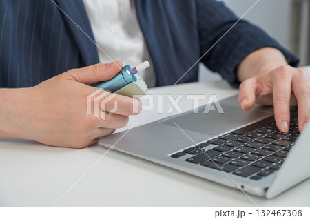 Business woman smoking an electronic cigarette while working on a laptop. Tobacco heating system.  132467308