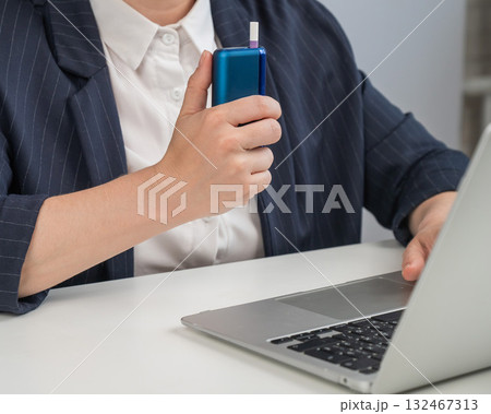Business woman smoking an electronic cigarette while working on a laptop. Tobacco heating system. Business woman smoking an electronic cigarette while working on a laptop. Tobacco heating system. 132467313