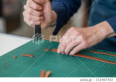 Woman tanner processes the edges of a leather belt in a workshop. Woman tanner processes the edges of a leather belt in a workshop. 132467342
