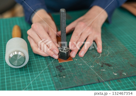 Woman tanner processes the edges of a leather belt in a workshop. Woman tanner processes the edges of a leather belt in a workshop. 132467354