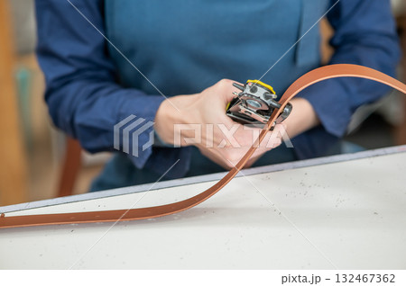 A woman makes holes in a leather belt. Leatherworker's workshop.  132467362