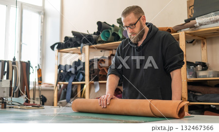 Caucasian bearded man working as a tanner in a workshop. Caucasian bearded man working as a tanner in a workshop. 132467366