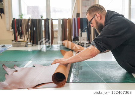 Caucasian bearded man working as a tanner in a workshop. Caucasian bearded man working as a tanner in a workshop. 132467368