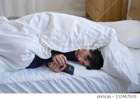 布団に包まってスマホを使う20代男性 布団に包まってスマホを使う20代男性 132467630