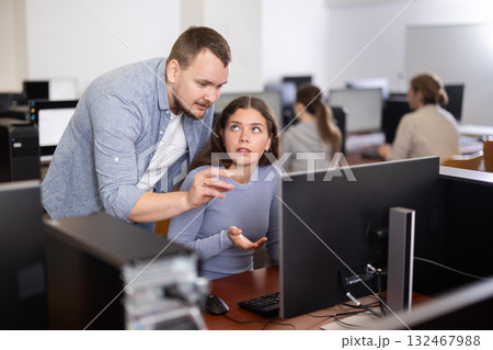During computer lesson, male teacher helps girl student complete difficult task During computer lesson, male teacher helps girl student complete difficult task 132467988