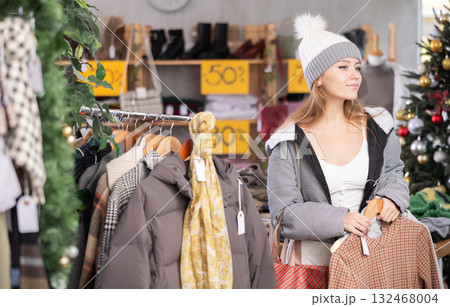 Young woman in hat choosing a sweater on Christmas tree background 132468004