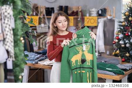 Girl client looks at products in store, looks closely at sweater, picks up wardrobe item 132468108