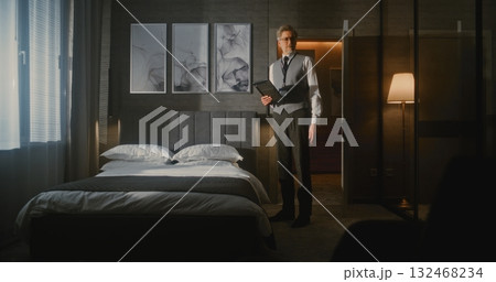 Mature Hotel Manager in Professional Business Attire Meticulously Checks and Photographs Bed Mature Hotel Manager in Professional Business Attire Meticulously Checks and Photographs Bed 132468234