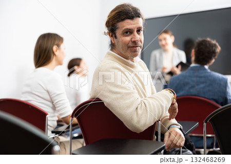 Portrait of smiling man participating in psychological trainings while sitting near employees in classroom 132468269