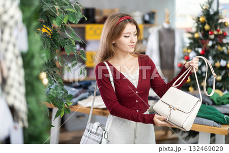 woman in a warm sweater chooses a handbag against the background of a Christmas tree 132469020