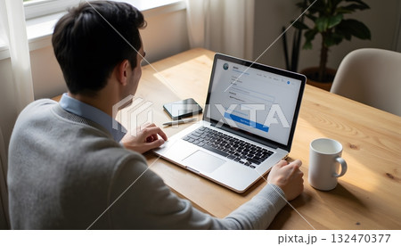 Young Man Working on Laptop in Modern Home Office with Coffee and Notepad 132470377