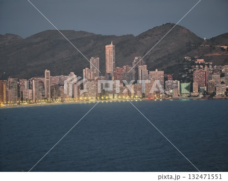 warm evening coastal cityscape, twilight glow reflecting on calm ocean near illuminated walkway 132471551
