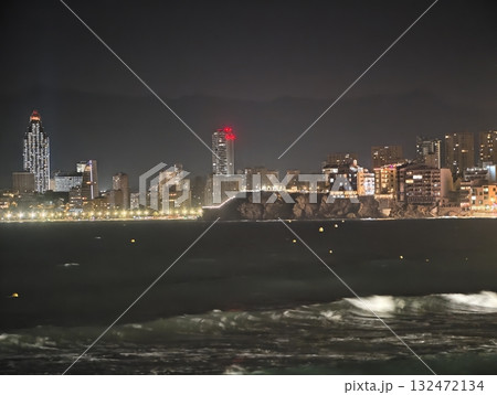 lively street by ocean surf, crowded urban promenade illuminated with lively night activities 132472134