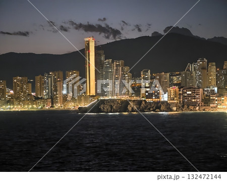 seaside night skyline, lively boulevard stretches below shimmering water with luminous tower 132472144